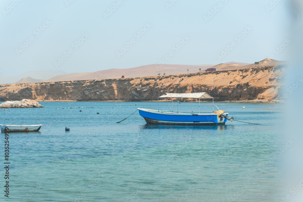 Fototapeta premium A blue boat is floating in the ocean near a rocky shore