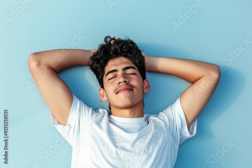 Serene Hispanic Young Man Relaxing on Floor with Arms Behind Head on Light Blue Background, Copy Space Above
