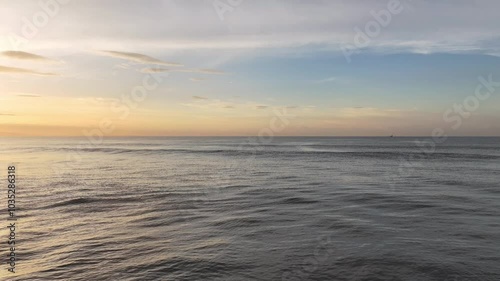 早朝の海岸、波打ち際から沖に向かって低空で飛行するドローン