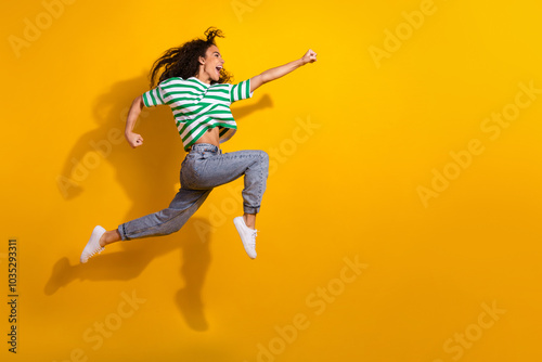 Full body portrait of nice young girl jump run empty space wear striped t-shirt isolated on yellow color background