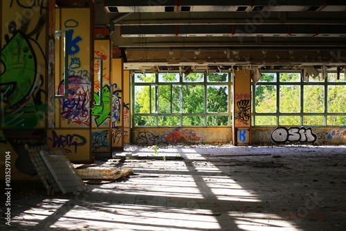 Graffiti-covered walls illuminated by sunlight in an abandoned space with broken windows and decay