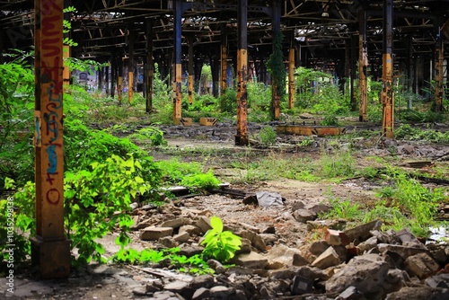 Abandoned industrial structure with rusted pillars overrun by vegetation and graffiti