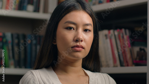 Serious concentrated asian woman girl student teenager businesswoman business lady teacher customer nod head approve agree looking at camera with piercing stern gaze posing indoors near bookshelf