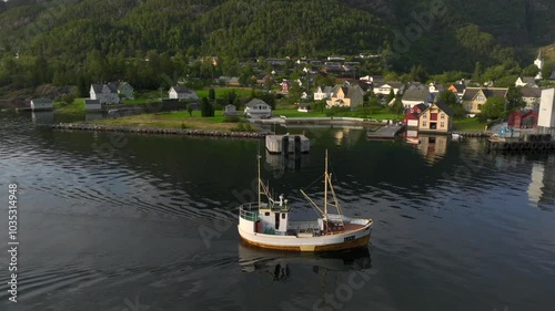 A Small Fishing Ship moves slowly in the still fjord waters in Jondal, Norway. Aerial Evening Sunset time Shot. photo