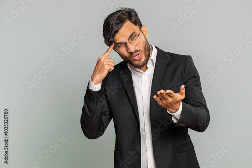 You are crazy, out of mind. Confused Indian businessman pointing at camera and showing stupid gesture, blaming asking some idiot for insane plan, bullying. Arabian man isolated on gray background photo