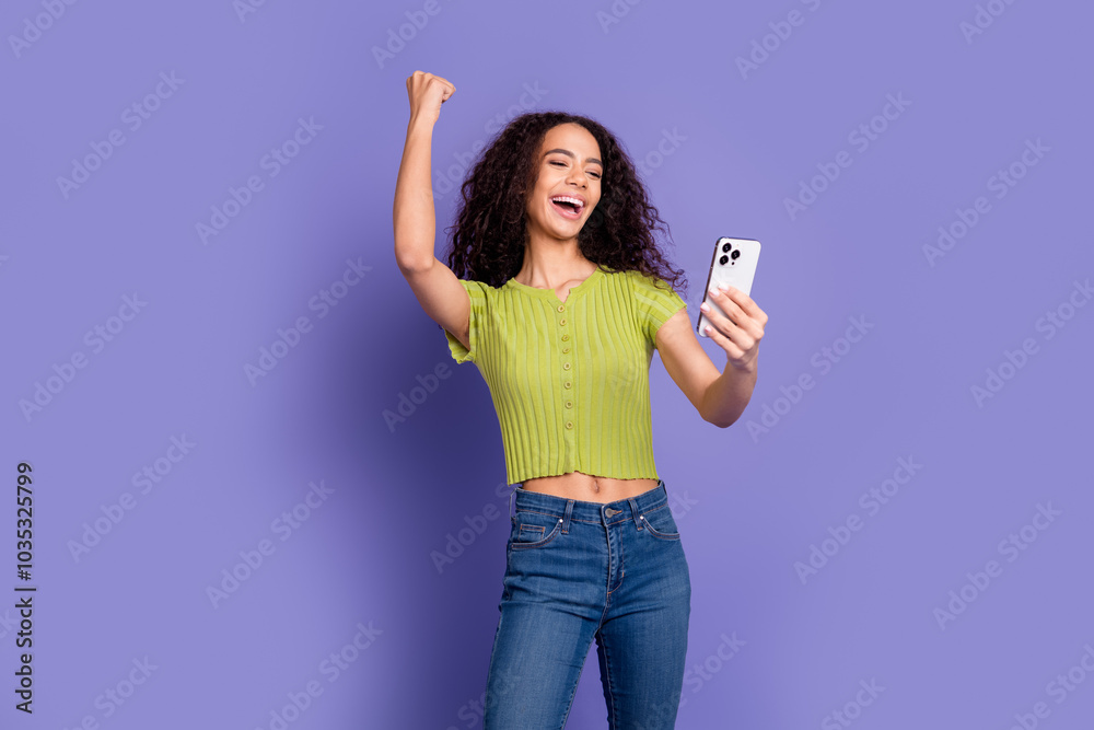 Photo portrait of lovely teen lady hold device winning dressed stylish green garment isolated on purple color background Photo portrait of lovely teen lady hold device winning dressed stylish green garment isolated on purple color background