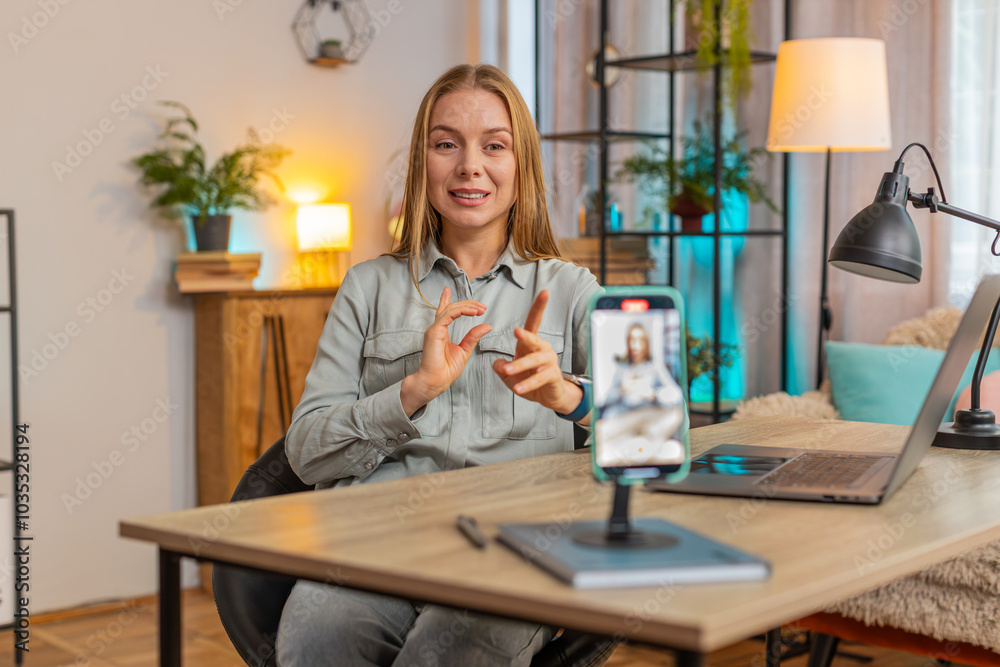 Smiling Caucasian businesswoman sitting at table before smartphone fixed on tripod record motivation training webinar on web camera. Video blogger influencer broadcast live speech using cell phone. Smiling Caucasian businesswoman sitting at table before smartphone fixed on tripod record motivation training webinar on web camera. Video blogger influencer broadcast live speech using cell phone.