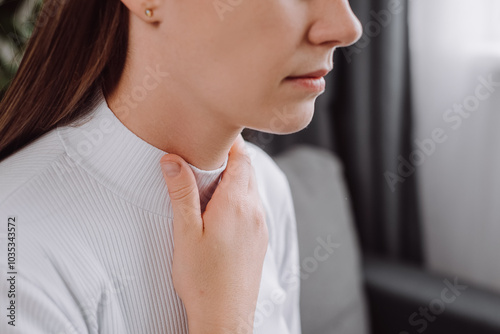 Close up of sick young caucasian woman with sore throat sitting on sofa, pain thyroid gland on neck or disease reflux, acid of suffer people. Medical and healthcare. Sickness in inflaming concept