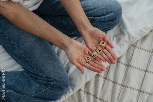 A person sitting on a bed holding wooden letter tiles to form the word 'pist'