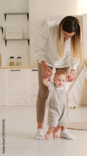 mom teaches the baby to walk at home, the baby boy learns to walk by taking the first steps holding his mother's hand