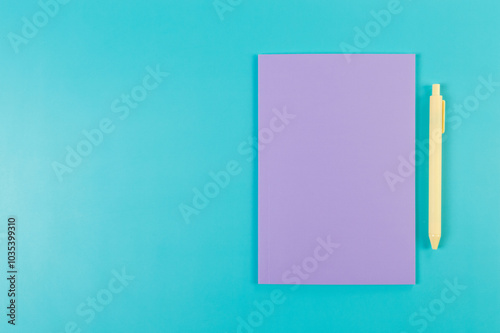 Top view of purple notebook, yellow pen on blue background. School, office wallpaper. Flat lay, copy space.