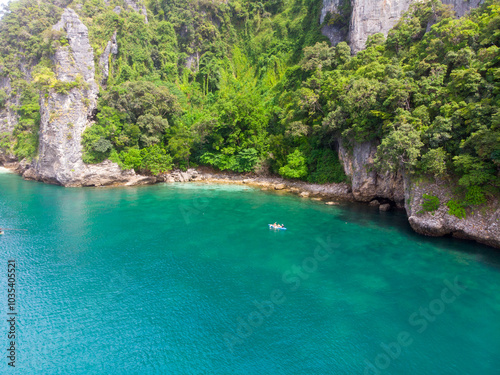 A serene cove with clear turquoise water surrounded by lush greenery and rocky cliffs.