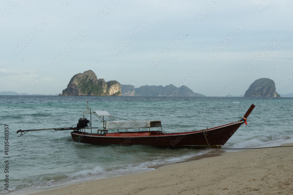 Fototapeta premium A solitary boat rests on a tranquil beach with distant islands in the background.