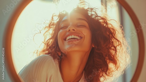 A young woman with curly hair beams with joy as sunlight illuminates her face in a bright, welcoming indoor space. The warm glow highlights her cheerful expression and creates a serene atmosphere.