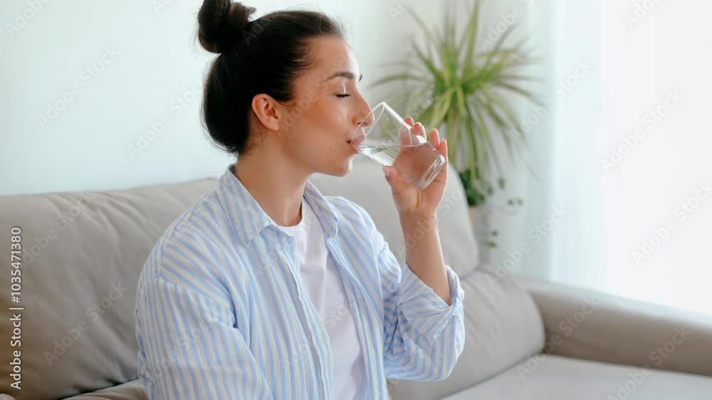 Happy positive arabian or indian brunette woman in casual clothes is drinking a glass cup of clean water on the morning, while sits in a couch in living room. Healthy life style concept Happy positive arabian or indian brunette woman in casual clothes is drinking a glass cup of clean water on the morning, while sits in a couch in living room. Healthy life style concept