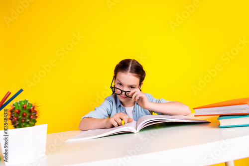 Photo of cute adorable clever girl wear trendy clothes sit table write hometask isolated on yellow color background photo