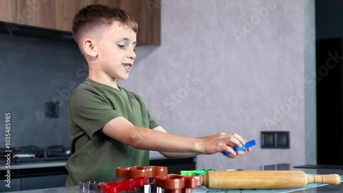 Little boy making cookies using cookie cutters and dough in the kitchen at home.