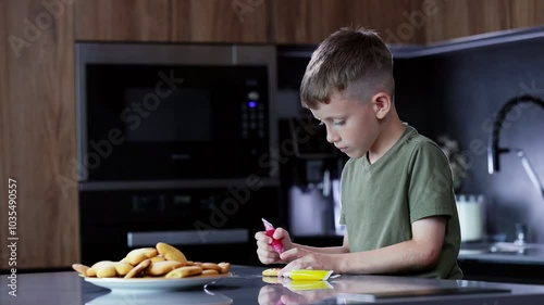 Cute boy decorating gingerbread cookies at home kitchen