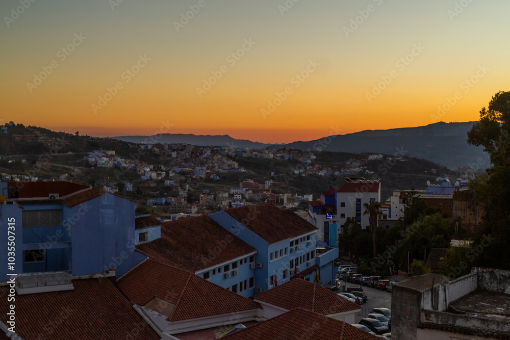 View of colorful rooftops and buildings at sunset with mountains in the background, Chefchaouen, Morocco. View of colorful rooftops and buildings at sunset with mountains in the background, Chefchaouen, Morocco.
