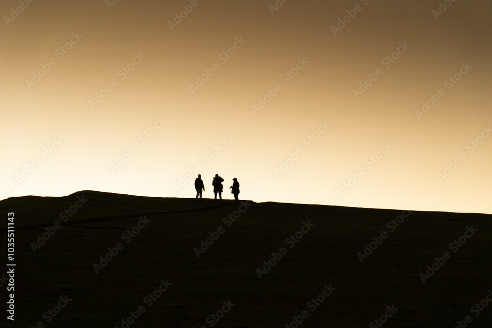 View of silhouettes of three people on a rugged cliff during sunset, Seven Sisters Cliffs, Eastbourne, United Kingdom. View of silhouettes of three people on a rugged cliff during sunset, Seven Sisters Cliffs, Eastbourne, United Kingdom.