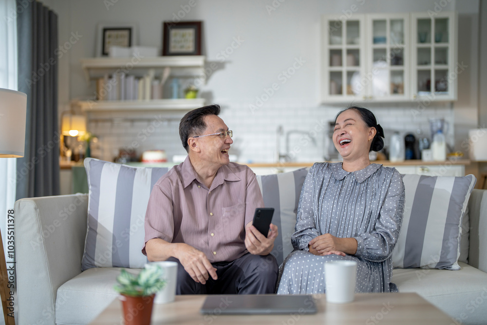 An elderly couple sits together in their cozy living room, smiling and enjoying a moment as they look at something on a smartphone. Their warmth and affection capture a peaceful home atmosphere. An elderly couple sits together in their cozy living room, smiling and enjoying a moment as they look at something on a smartphone. Their warmth and affection capture a peaceful home atmosphere.