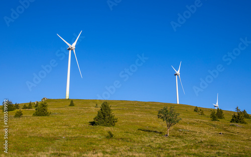 View of wind turbines on a sunny mountain pasture with trees and hills, Handalm, Austria. photo