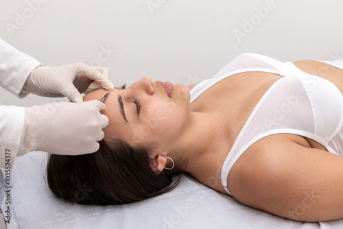 young woman on a table in a beauty center performing a beauty treatment for facial skin with a scalpel using the dermaplaning technique