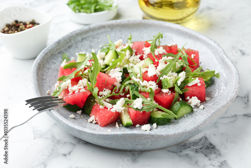 Delicious watermelon salad with feta cheese, cucumber and arugula served on white marble table, closeup