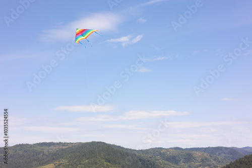 One colorful kite flying in mountains under blue sky