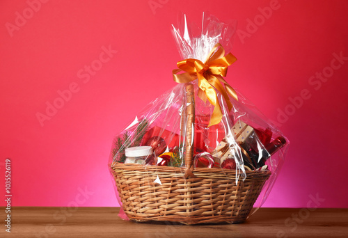 Wicker gift basket with wine on wooden table against pink background photo