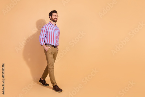 Full length photo of handsome young guy walking empty space dressed stylish striped formalwear isolated on beige color background