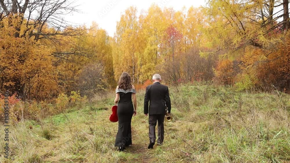 two musicians, a violinist and a trumpeter with musical instruments, walk away through the autumn forest two musicians, a violinist and a trumpeter with musical instruments, walk away through the autumn forest