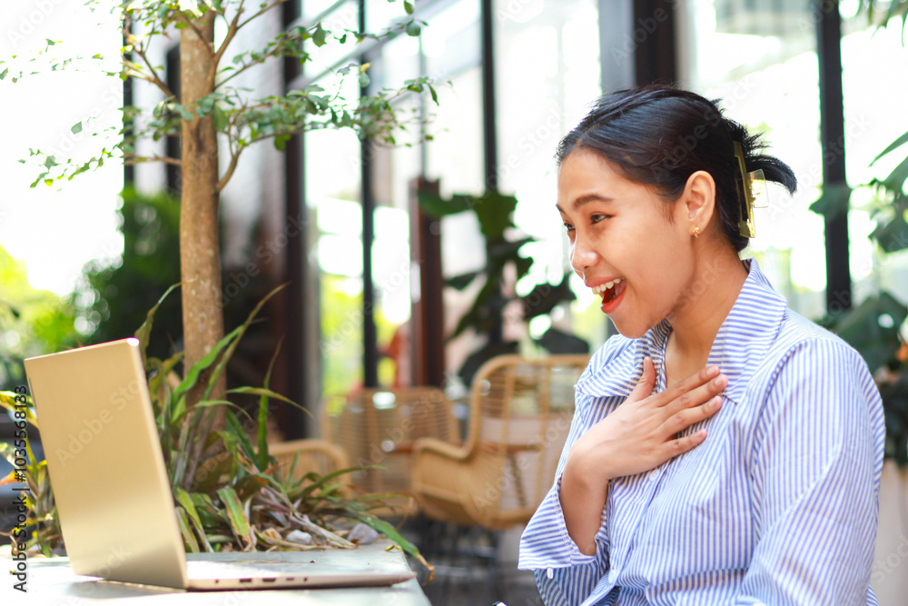 surprised asian business woman looking at laptop working from outdoor cafe touching her chest