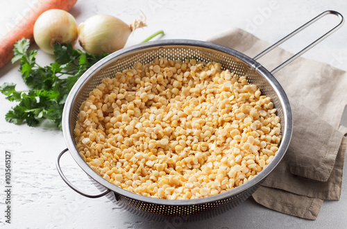 Yellow split soaked peas in a metal colander, onion, carrot and parsley, stage of cooking, on a light gray background photo