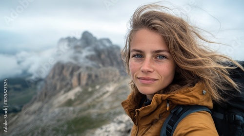 A young woman in a yellow jacket stands in front of majestic mountains under a cloudy sky, showcasing a spirit of adventure and exploration.