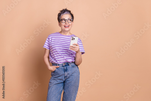 Photo of adorable woman wear striped trendy clothes hold modern gadget look empty space isolated on beige color background photo