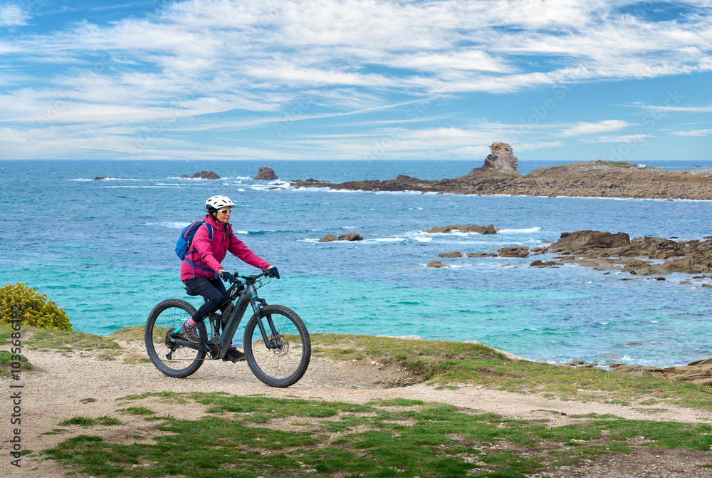 Obraz premium active senior woman cycling with her electric mountain bike at the rocky red granite cost next to Ploumanac'h, Côtes d'Armor,Brittany, France