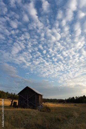 Dramatic cloudy ranch landscape, rural log cabin shack at sunset, western skyscape agriculture