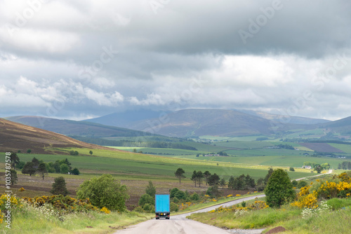 Panoramic drivers perspective of a road with truck in landscape with rolling green hills and dark clouds over the mountains leading to Dufftown, Keith, UK