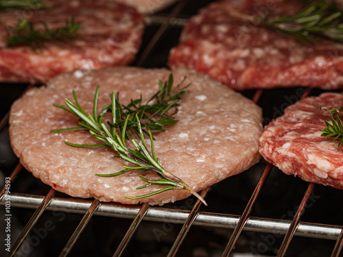 Seasoned burgers and steak cuts garnished with rosemary, grilling over hot coals photo