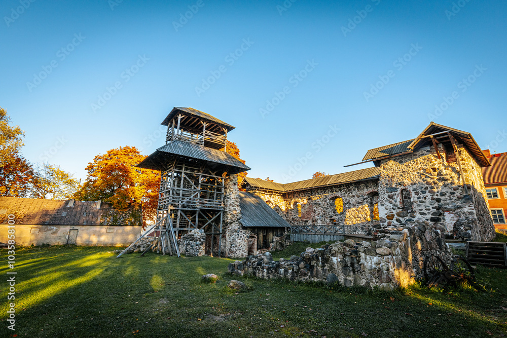 Fototapeta premium A historic stone fortress featuring wooden towers and platforms under a clear sky. Autumn foliage adds vibrant orange hues, enhancing the rustic charm of the ancient architecture.
