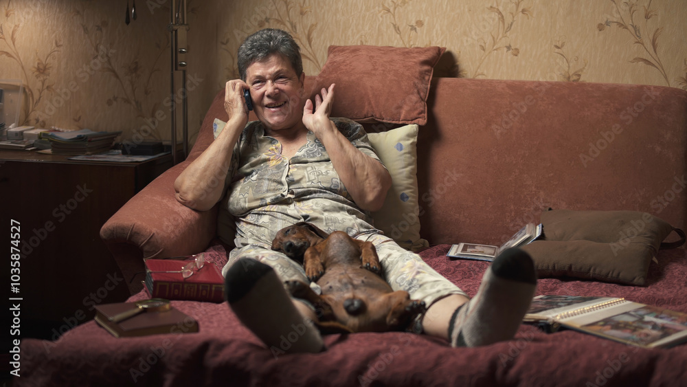Elderly woman sitting on sofa and talking on mobile phone, holding dachshund. Elderly woman sitting on sofa and talking on mobile phone, holding dachshund.