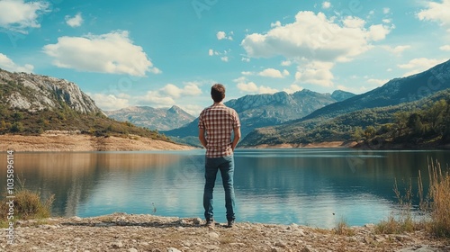 A young man taking in the scenery while standing close to a lake and a mountain.