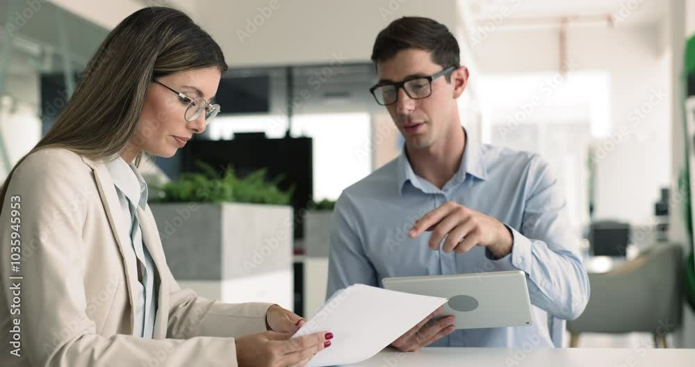 Two professionals engaged in business meeting and discussion, holding some documents using digital tablet met in modern office, review documents and reports. Collaboration, teamwork, decision-making