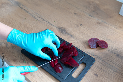 The photo shows hands in gloves cutting a beetroot on a cutting board.