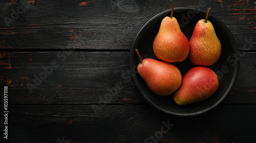 A top view of a bowl filled with ripe pears set against a black wooden background.






