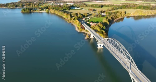 Aerial view of Lake Champlain Bridge during autumn, spanning the serene lake and connecting Crown Point, New York to Vermont, with fall foliage and distant mountain ranges under clear skies.
