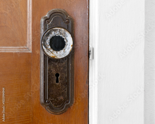 Close-up photo of an old glass doorknob on a scratched and worn metal plate with a skeleton key keyhole and unpainted wood door.