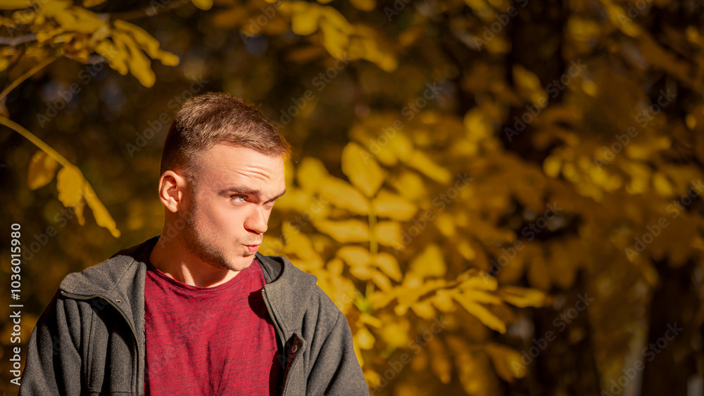A Young Man Making a Playful Expression Amid Golden Autumn Foliage During a Sunny Afternoon in a Picturesque Park Setting A Young Man Making a Playful Expression Amid Golden Autumn Foliage During a Sunny Afternoon in a Picturesque Park Setting