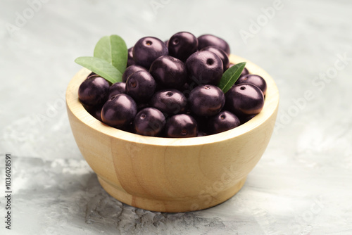 Ripe acai berries and leaves in bowl on grey textured table, closeup photo